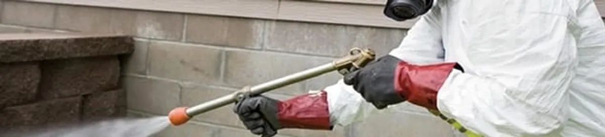 Pest control technician applying exterior insect treatment along a home foundation in Charleston, SC