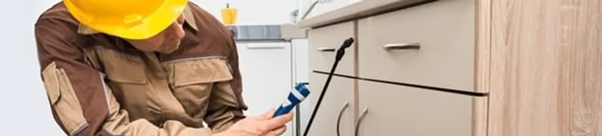 Roach exterminator applying treatment under kitchen cabinets in Charleston, SC